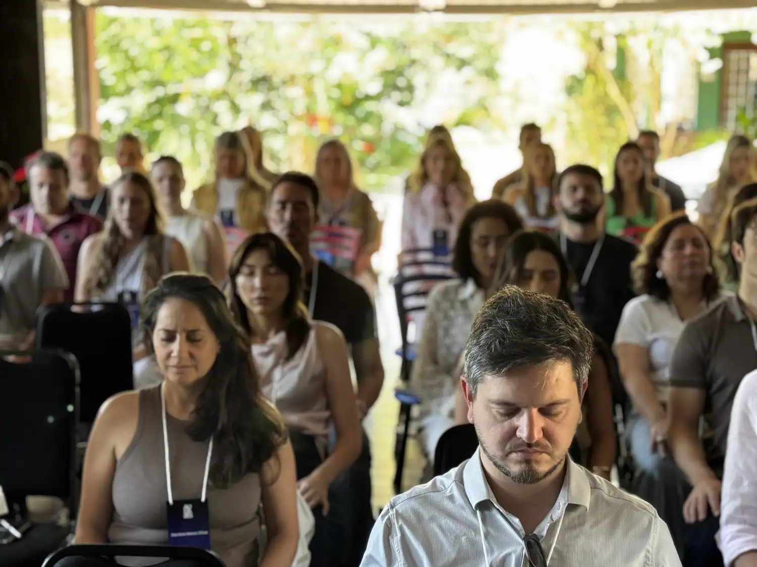 Turma inteira sentada em silêncio, de olhos fechados, durante uma prática coletiva ao ar livre.