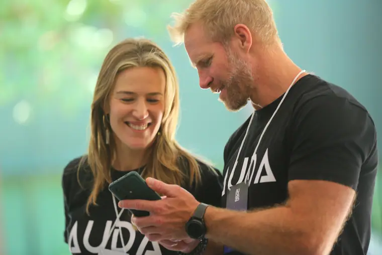 Dois participantes sorrindo enquanto olham algo no celular.