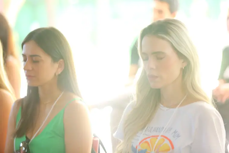 Duas participantes de olhos fechados durante uma prática, contra a luz do jardim.