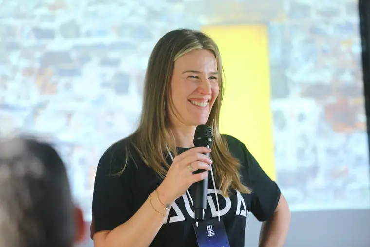 Facilitadora sorrindo com microfone na mão durante a condução de uma mentoria.