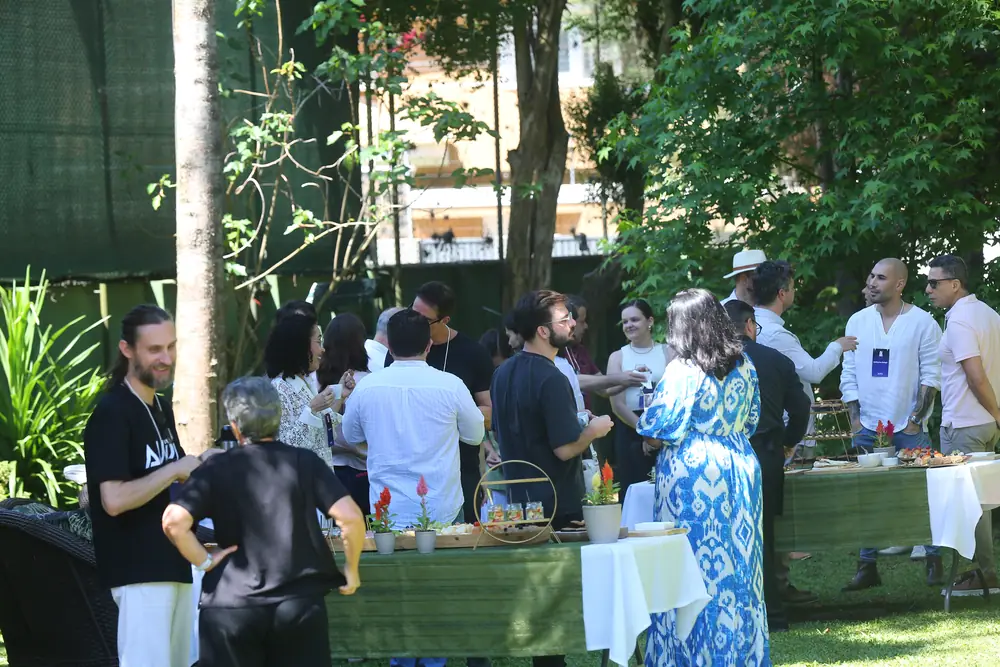 Intervalo no jardim, participantes em pé conversando em volta das mesas.